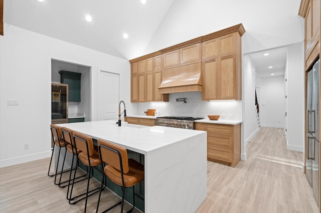 kitchen with light hardwood / wood-style floors, sink, range hood, and an island with sink