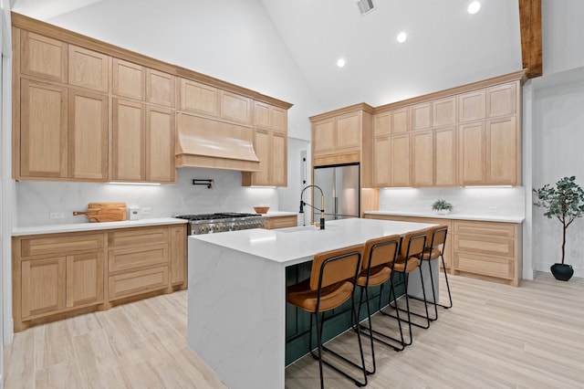 kitchen with high vaulted ceiling, a kitchen bar, a kitchen island with sink, stainless steel appliances, and custom range hood