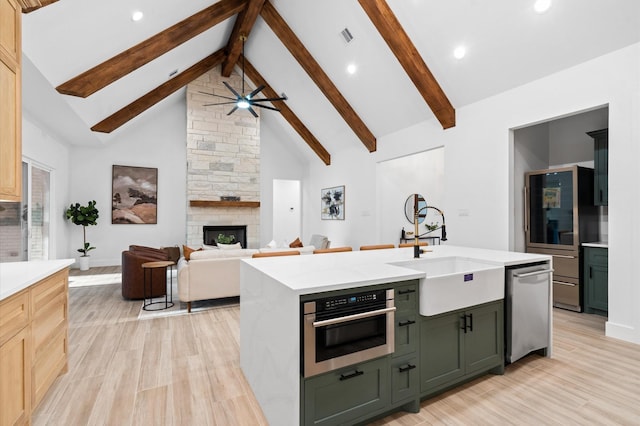 kitchen with appliances with stainless steel finishes, high vaulted ceiling, sink, a center island with sink, and beam ceiling