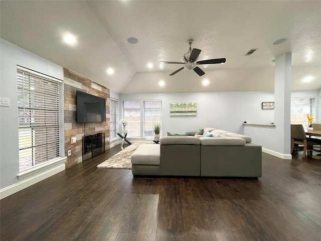 living room featuring lofted ceiling, a tiled fireplace, dark wood-type flooring, and ceiling fan