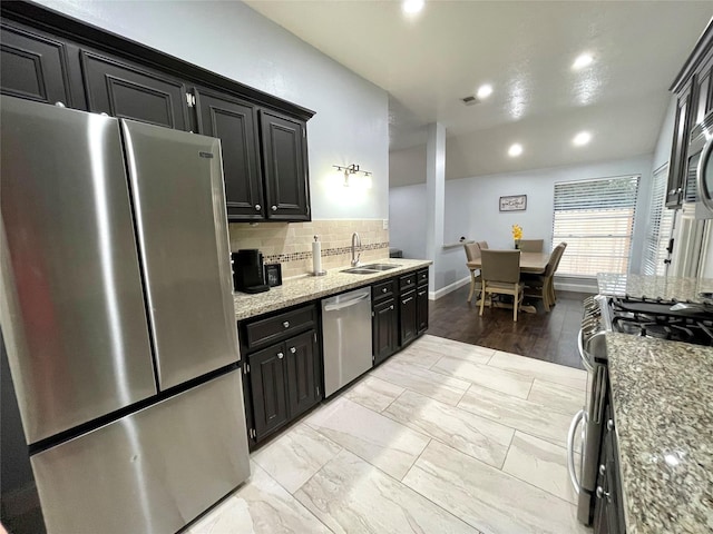 kitchen with stainless steel appliances, sink, backsplash, and light stone counters