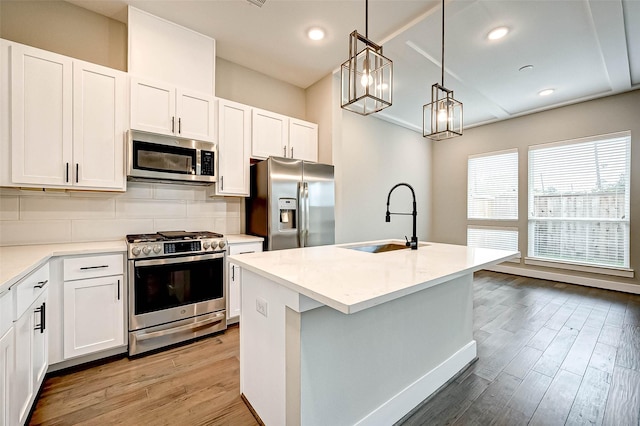 kitchen with sink, a center island with sink, pendant lighting, stainless steel appliances, and white cabinets