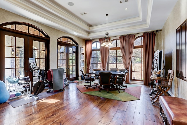 dining room featuring hardwood / wood-style flooring, an inviting chandelier, a tray ceiling, ornamental molding, and french doors