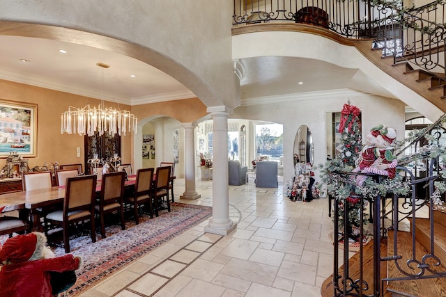 foyer featuring crown molding, a towering ceiling, decorative columns, and a notable chandelier