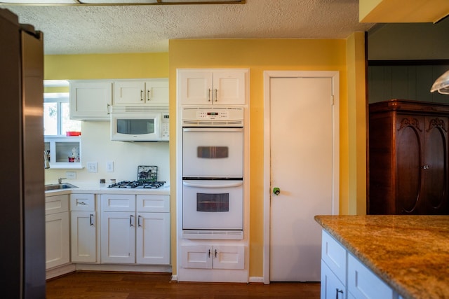 kitchen with white cabinetry, dark hardwood / wood-style floors, a textured ceiling, and white appliances