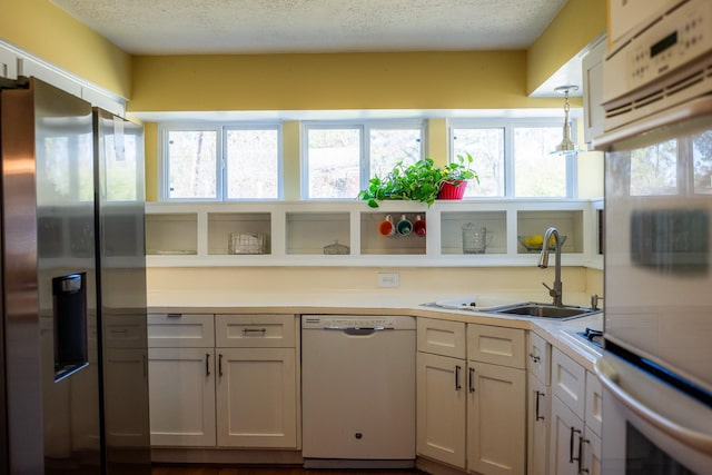 kitchen featuring white appliances, decorative light fixtures, sink, and white cabinets