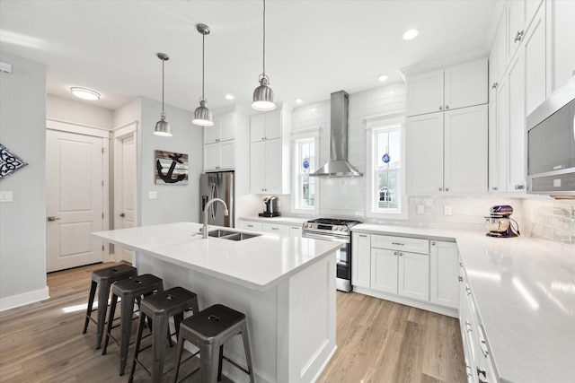 kitchen with appliances with stainless steel finishes, wall chimney exhaust hood, a center island with sink, and white cabinets