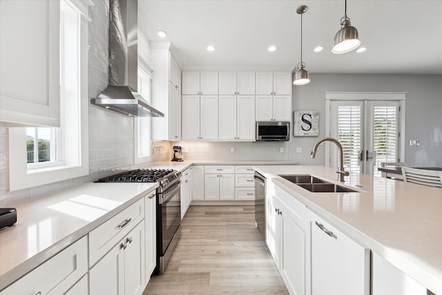 kitchen featuring sink, wall chimney range hood, stainless steel appliances, white cabinets, and decorative light fixtures