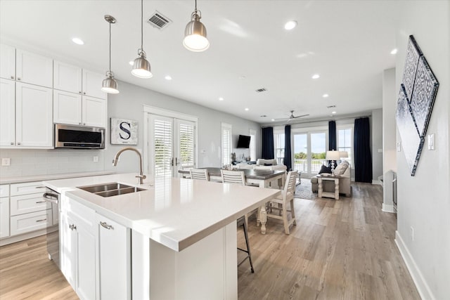 kitchen with sink, white cabinetry, tasteful backsplash, an island with sink, and pendant lighting