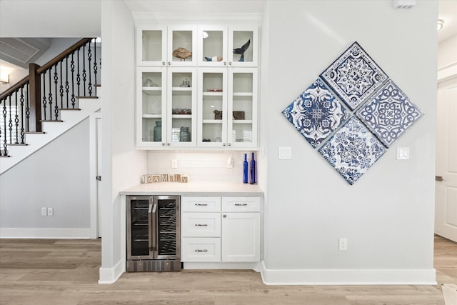 bar featuring white cabinets, light wood-type flooring, beverage cooler, and backsplash