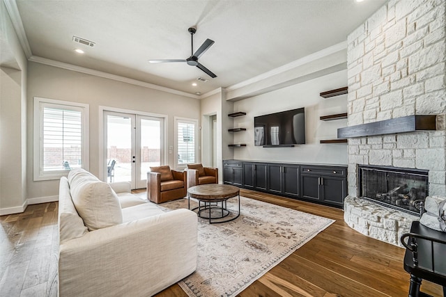 living room with crown molding, a stone fireplace, french doors, and plenty of natural light