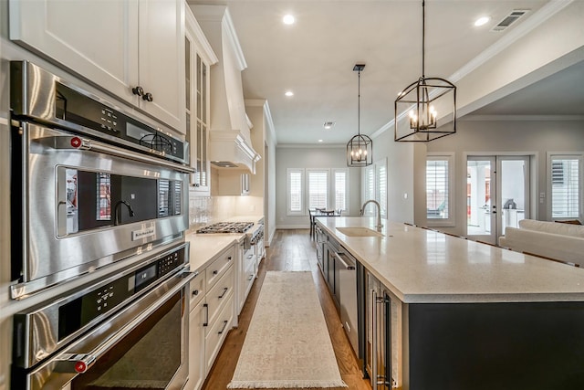 kitchen with white cabinetry, sink, decorative light fixtures, and a center island with sink