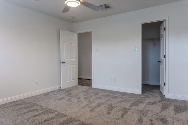 unfurnished bedroom with a spacious closet, a closet, ceiling fan, and dark colored carpet