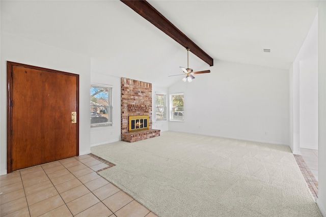 unfurnished living room featuring ceiling fan, a fireplace, lofted ceiling with beams, and light tile patterned floors