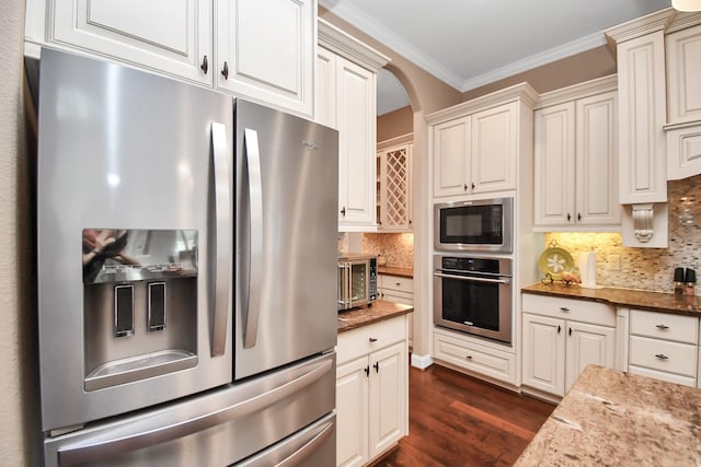 kitchen with dark stone countertops, ornamental molding, appliances with stainless steel finishes, dark hardwood / wood-style flooring, and backsplash