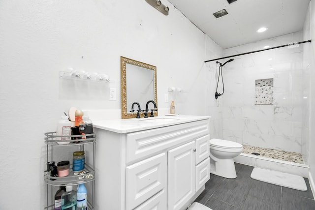 bathroom with a tile shower, vanity, and toilet