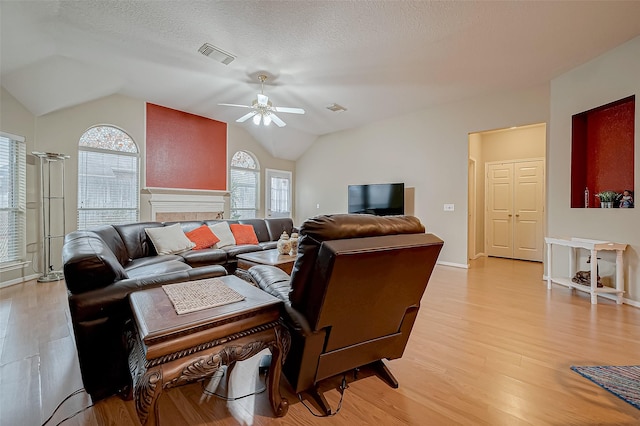 living room with light hardwood / wood-style flooring, ceiling fan, vaulted ceiling, and a textured ceiling