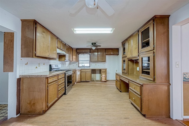 kitchen with stainless steel gas range oven, light wood-type flooring, ceiling fan, decorative backsplash, and paneled dishwasher