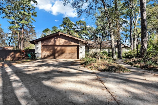 view of front of home with a garage, driveway, stone siding, and fence