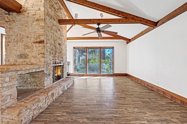 unfurnished living room featuring dark wood finished floors, lofted ceiling with beams, a ceiling fan, a stone fireplace, and baseboards