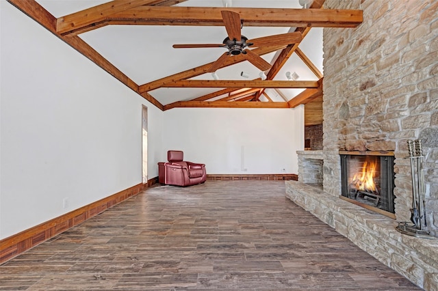 unfurnished living room featuring lofted ceiling with beams, dark hardwood / wood-style flooring, a stone fireplace, and ceiling fan