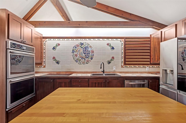 kitchen with decorative backsplash, lofted ceiling with beams, appliances with stainless steel finishes, wooden counters, and a sink