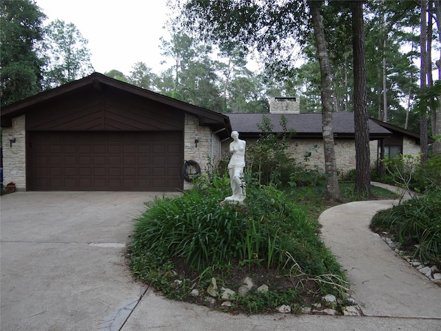 view of front of house with a garage, concrete driveway, stone siding, a chimney, and roof with shingles