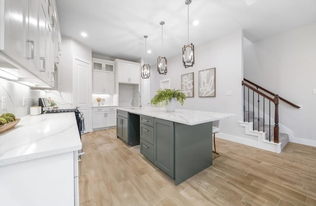 kitchen featuring a kitchen island with sink, hanging light fixtures, white cabinetry, and light hardwood / wood-style floors