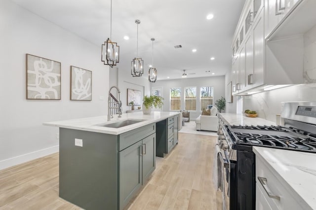 kitchen featuring sink, white cabinets, gas range, light stone countertops, and a center island with sink