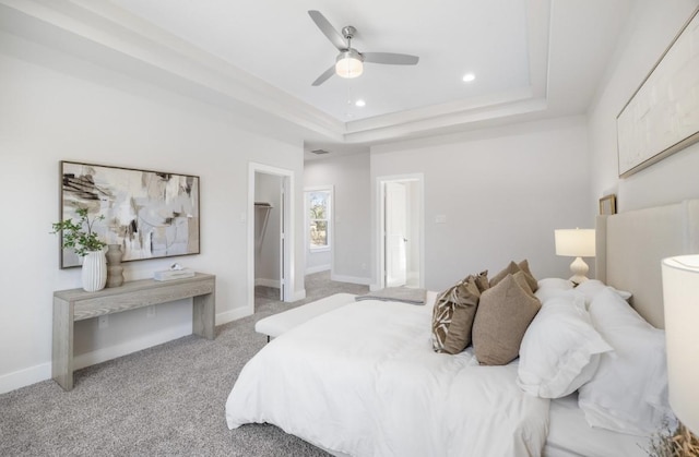 carpeted bedroom featuring a tray ceiling, a walk in closet, and ceiling fan