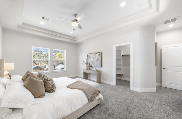 carpeted bedroom with a closet, a walk in closet, a raised ceiling, and ceiling fan