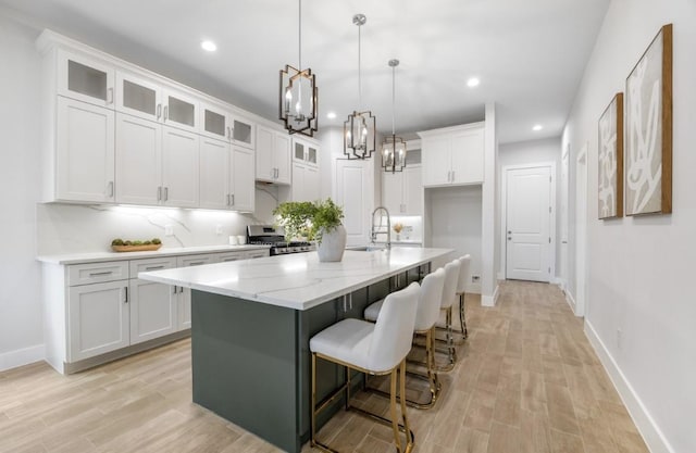 kitchen featuring stainless steel range oven, light stone countertops, an island with sink, and white cabinets