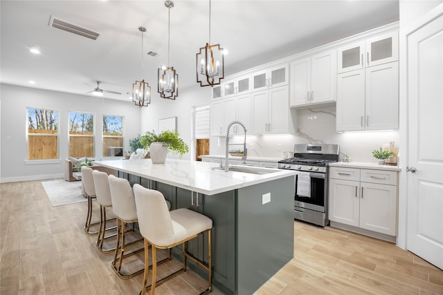 kitchen with sink, gas stove, white cabinetry, hanging light fixtures, and an island with sink