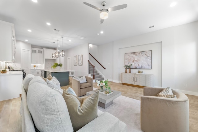 living room with sink, ceiling fan with notable chandelier, and light hardwood / wood-style flooring