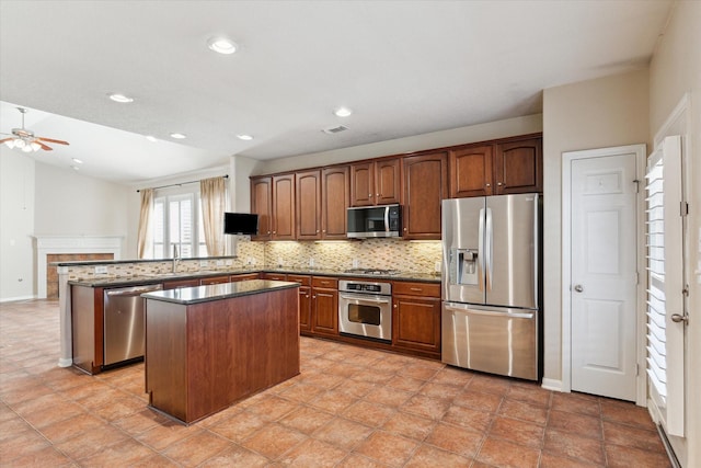 kitchen with decorative backsplash, a tiled fireplace, appliances with stainless steel finishes, a center island, and a peninsula