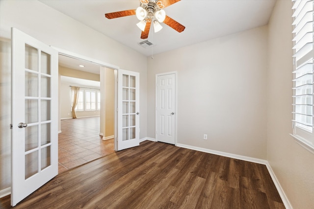 empty room with dark wood-style flooring, a ceiling fan, visible vents, baseboards, and french doors