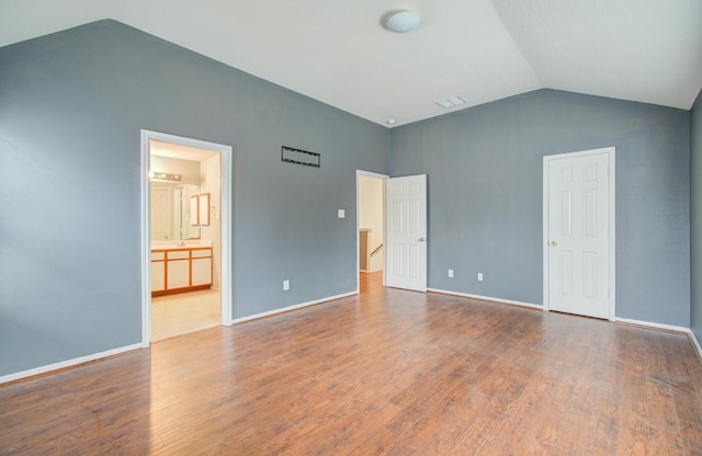 unfurnished bedroom with vaulted ceiling, connected bathroom, and hardwood / wood-style floors