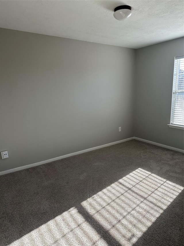 empty room featuring a textured ceiling, carpet flooring, and baseboards