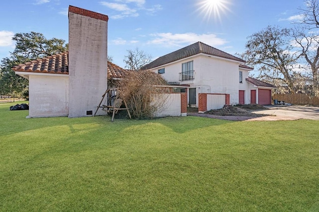 back of property with a garage, a balcony, and a lawn