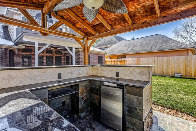 view of patio / terrace featuring a bar, ceiling fan, and exterior kitchen