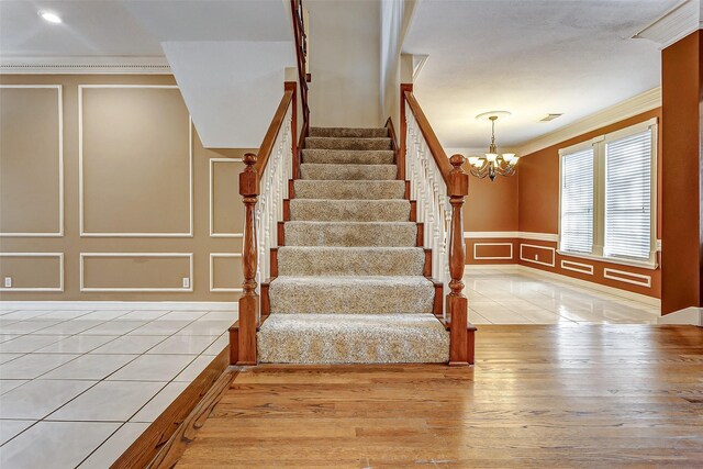 stairs with an inviting chandelier, ornamental molding, and tile patterned flooring