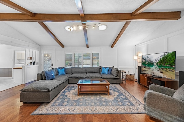 living room featuring vaulted ceiling with beams, a textured ceiling, wood finished floors, and a decorative wall