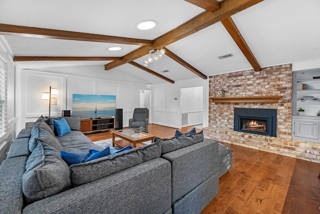 living room featuring built in features, vaulted ceiling with beams, a decorative wall, a brick fireplace, and wood finished floors