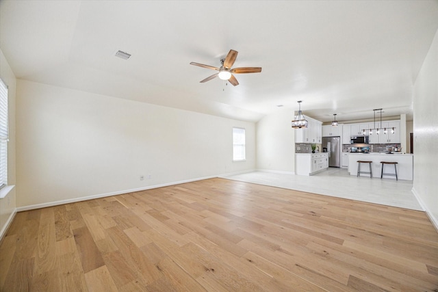 unfurnished living room featuring ceiling fan with notable chandelier, lofted ceiling, and light hardwood / wood-style floors