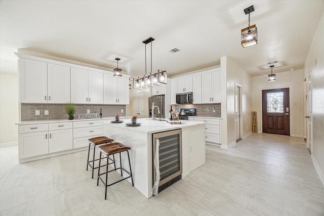 kitchen featuring hanging light fixtures, a center island with sink, stainless steel appliances, beverage cooler, and white cabinets