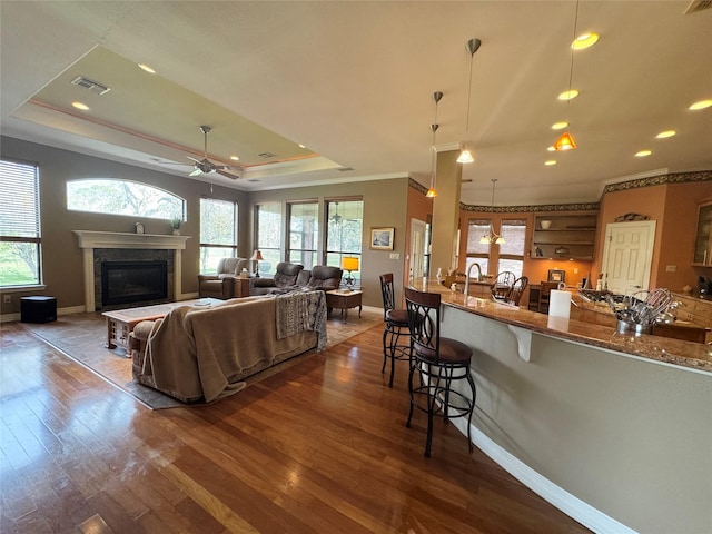 living room featuring dark wood-type flooring, ceiling fan, ornamental molding, and a tray ceiling