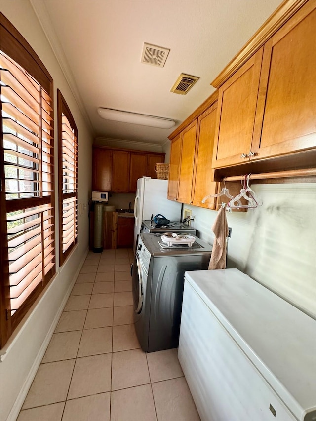 laundry room with cabinets, washing machine and dryer, light tile patterned floors, and crown molding