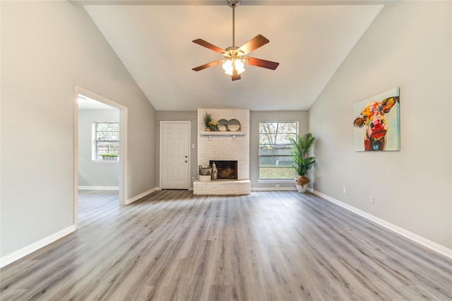 unfurnished living room featuring ceiling fan, plenty of natural light, a fireplace, and light wood-type flooring