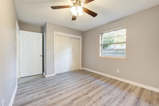 unfurnished bedroom with ceiling fan, a textured ceiling, a closet, and light wood-type flooring