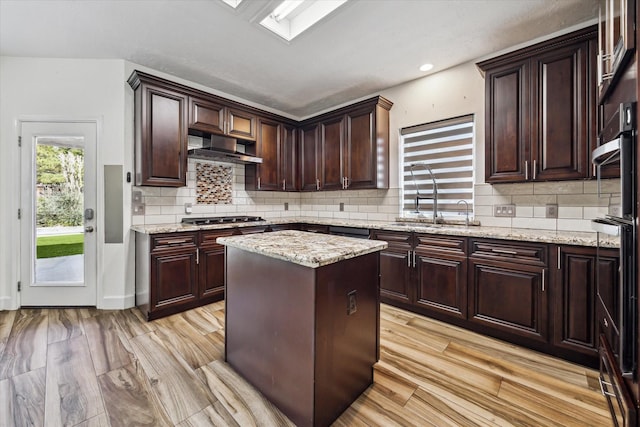 kitchen featuring stainless steel gas stovetop, sink, a center island, light stone counters, and light hardwood / wood-style floors